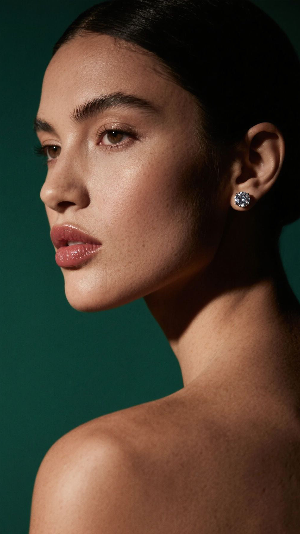 Woman wearing diamond earrings against a dark green background